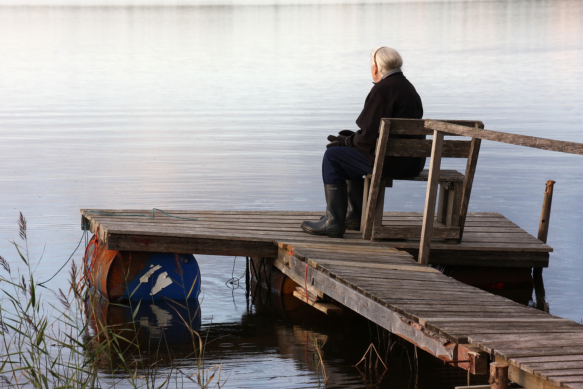 Eine alte Frau sitzt am Wasser und ist traurig.